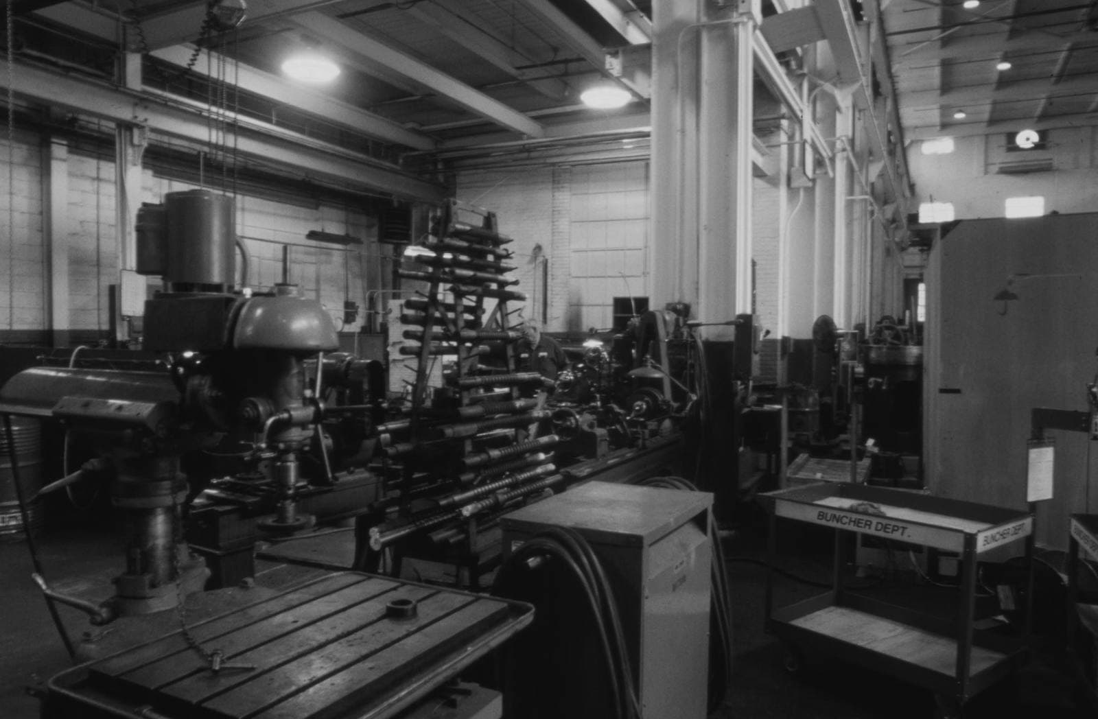 Radial drill press and milling machines with a rack of long steel rods in a dim machine shop bay