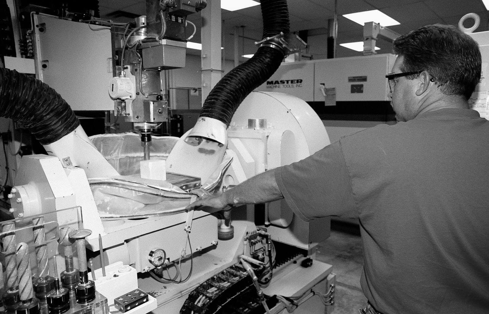 Machinist in an orange shirt operating a 5-axis CNC milling machine cutting a block of insulation tile